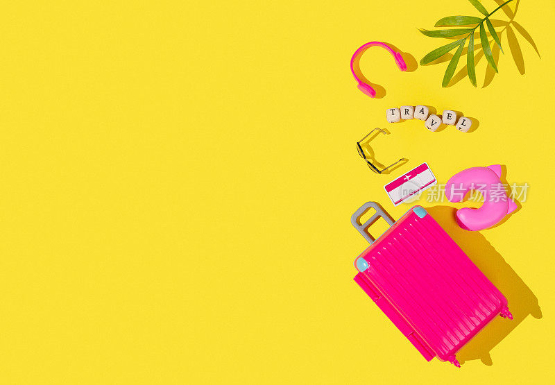 黄色背景上平放着粉红色的玩具行李箱和旅行配件。旅行的概念。