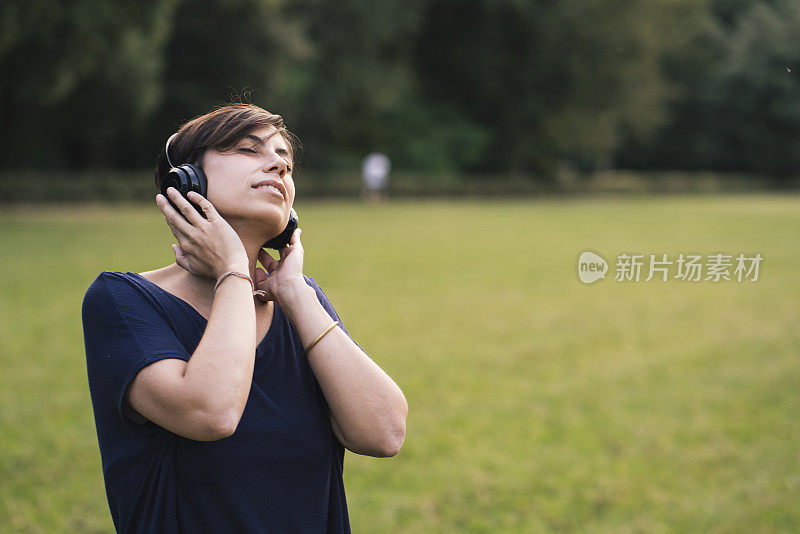 年轻的成年女子在公园里听音乐