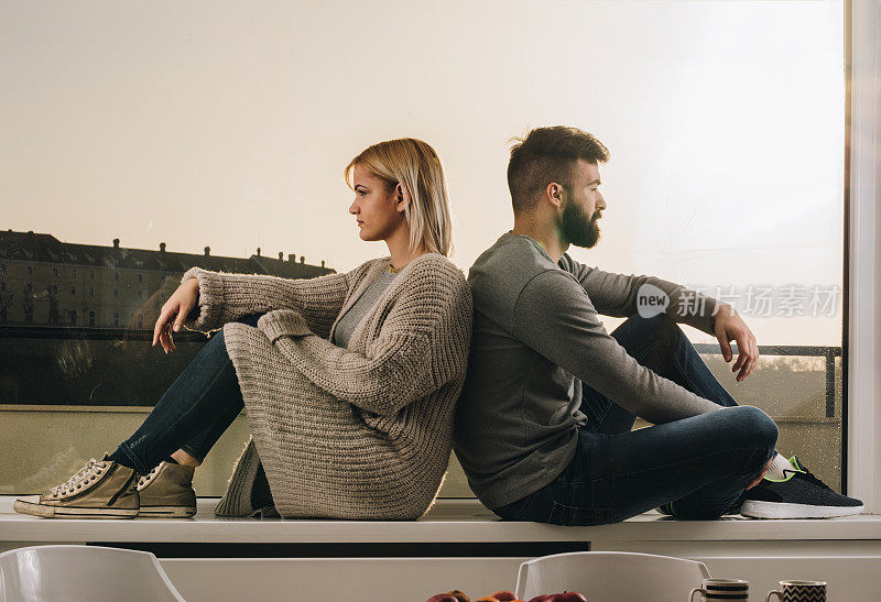 一对年轻夫妇背靠背坐在窗台上，但他们的关系出现了问题。
