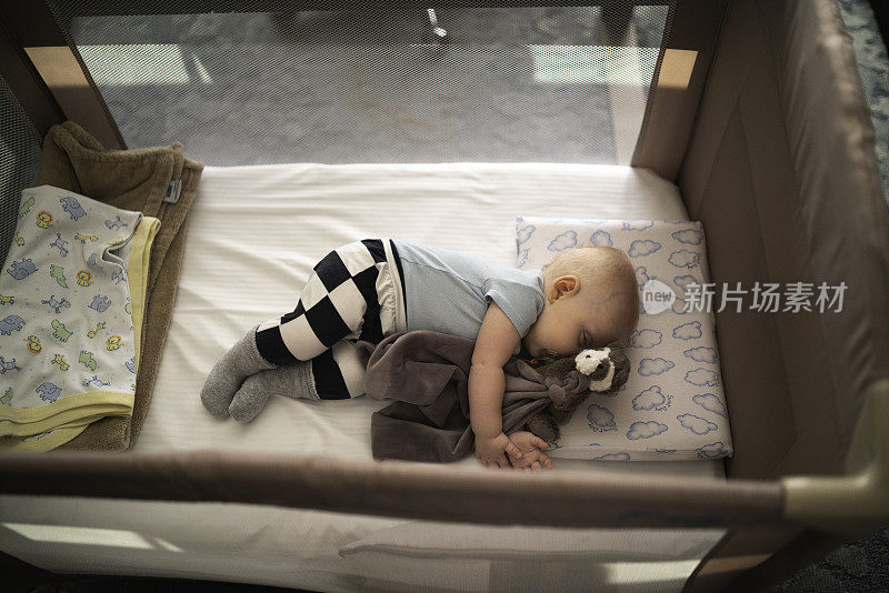 可爱的金发小男孩睡在婴儿床里