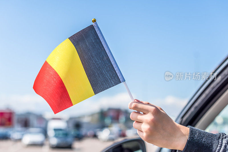 一个男孩拿着比利时国旗从打开的车窗在购物中心的停车场。概念
