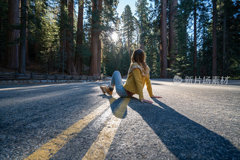 女孩坐在空旷的道路上，在森林中思考自然，享受公路旅行