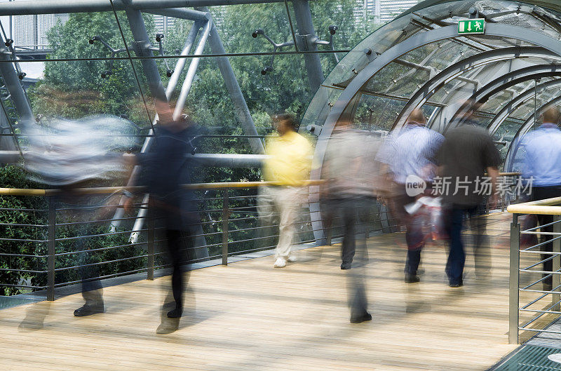 行人在现代玻璃建筑的人行道上行走，模糊的运动