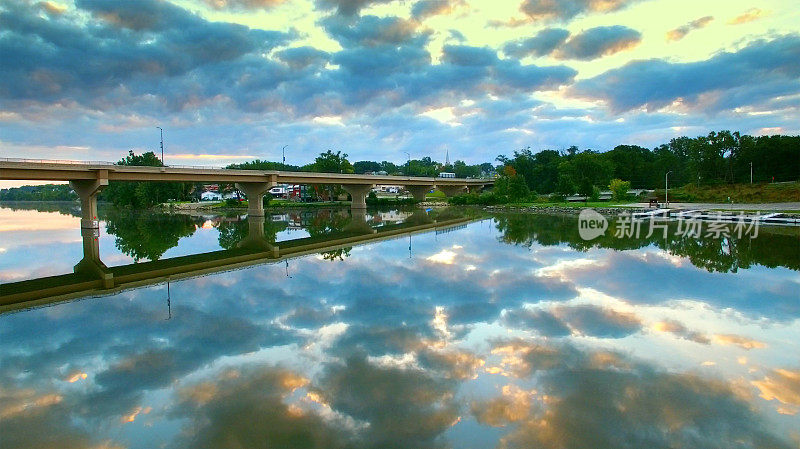 多云的黎明天空倒映在风景桥下宁静的河面上