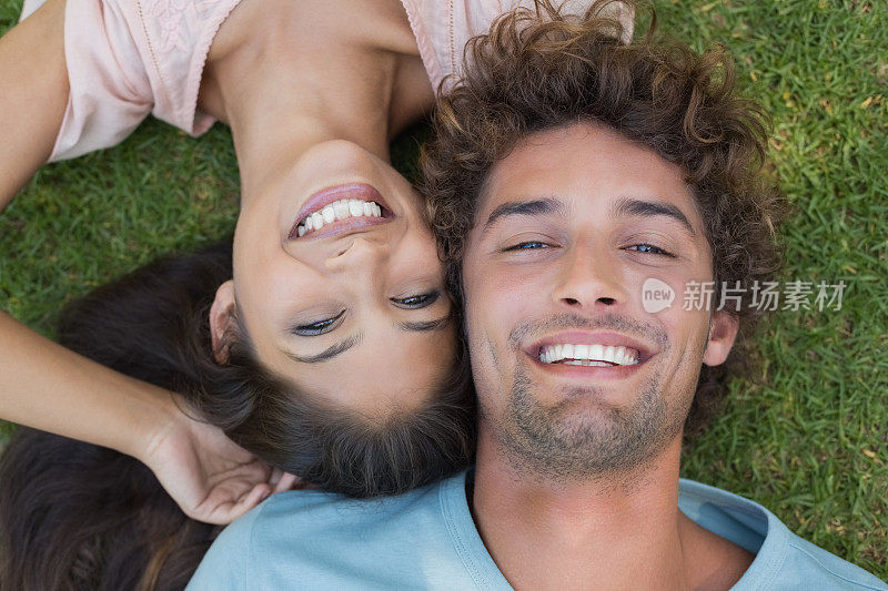 一对年轻夫妇躺在草地上对着镜头微笑