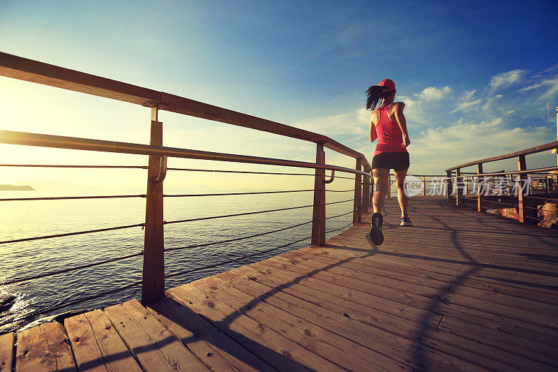 年轻的健身妇女跑步在日出的海滨木板路