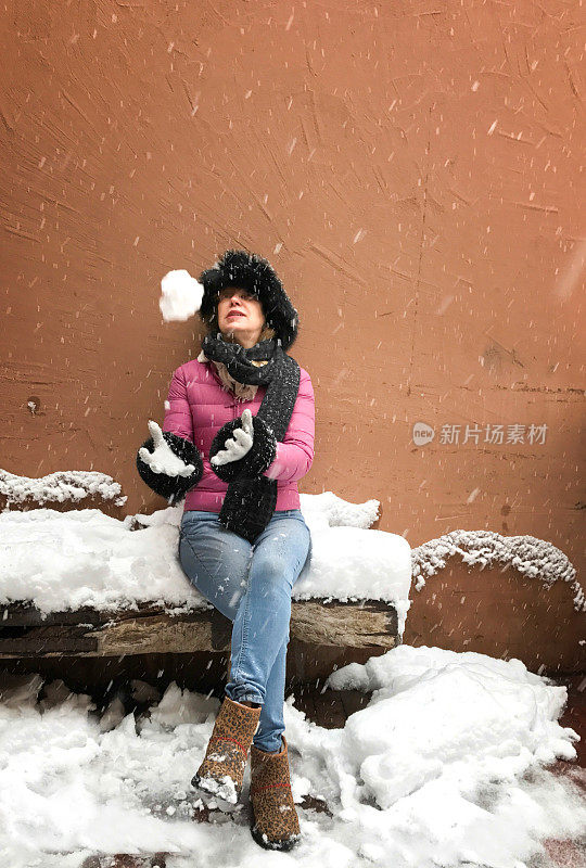 下雪:一个女人坐在下雪的长凳上扔雪球
