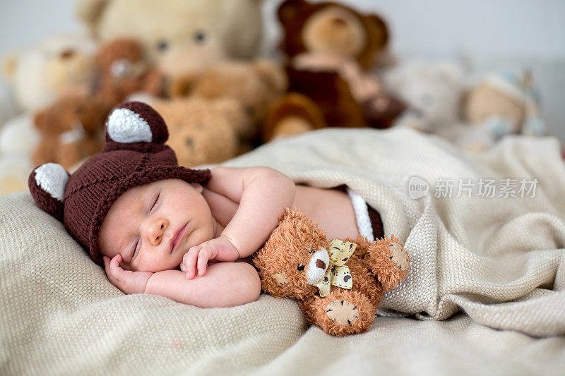 刚出生的小男孩，和泰迪熊一起睡在家里的床上