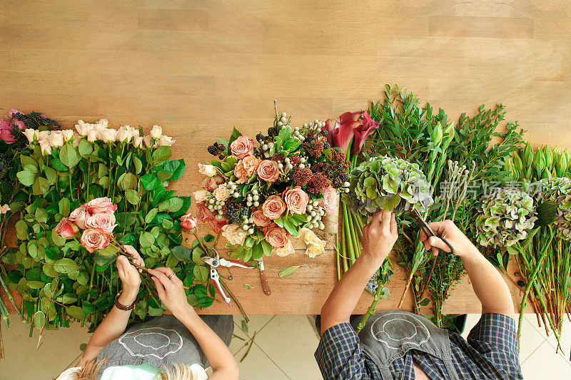 花店和花店助理送货制作玫瑰花束，桌面俯视