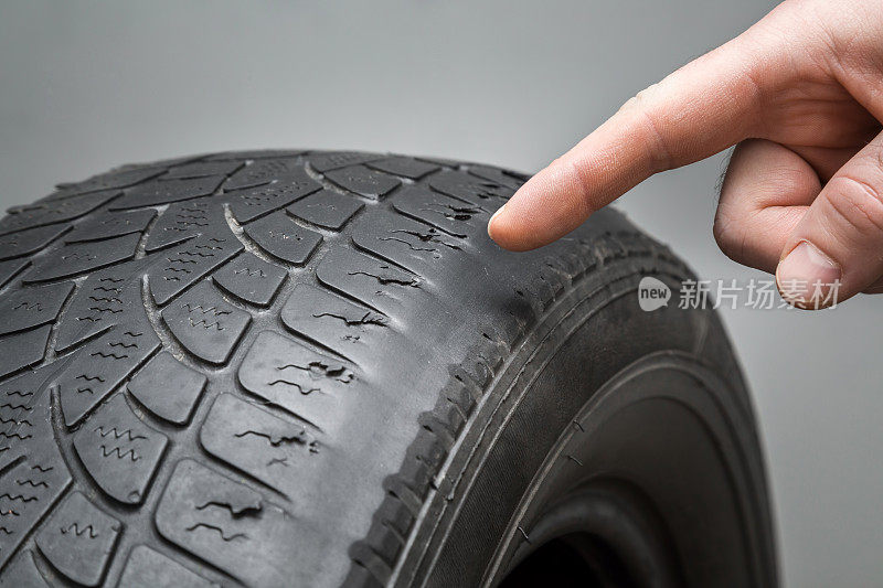 男人的手指指着旧的，损坏和磨损的黑色轮胎胎面。改变时间。轮胎胎面问题和解决方案的概念。