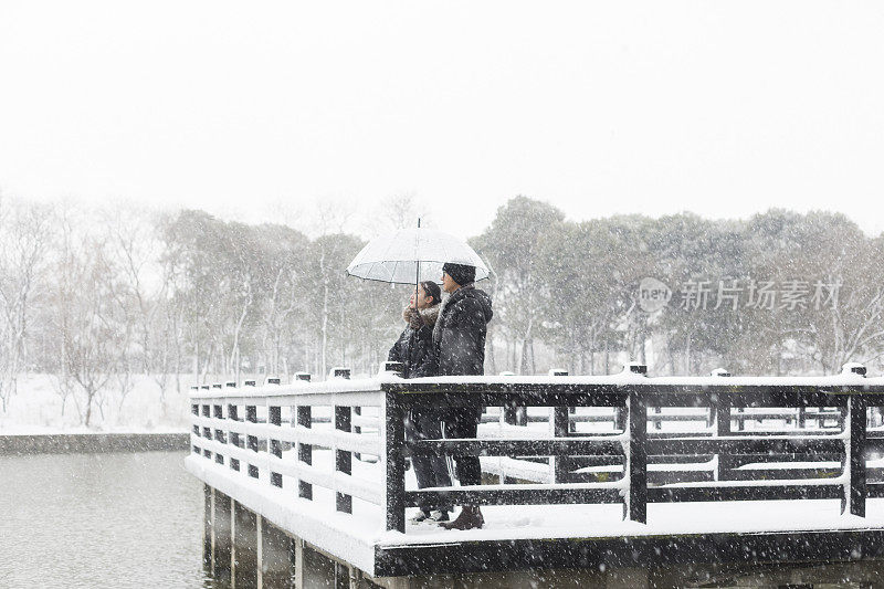 一对情侣撑着伞站在白雪覆盖的木桥上