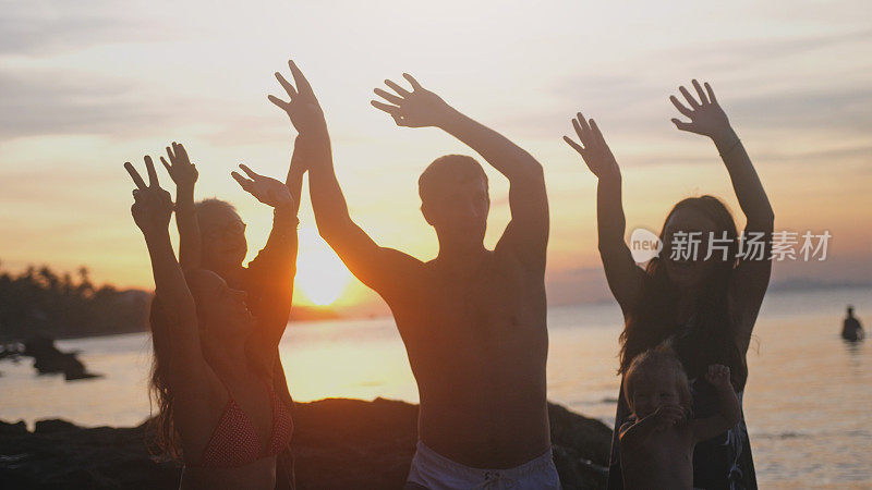 一群幸福的家庭享受夏天日落升起他们的手在热带海滩上