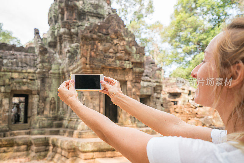 一名年轻女子在柬埔寨吴哥窟的寺庙观光中用智能手机拍照