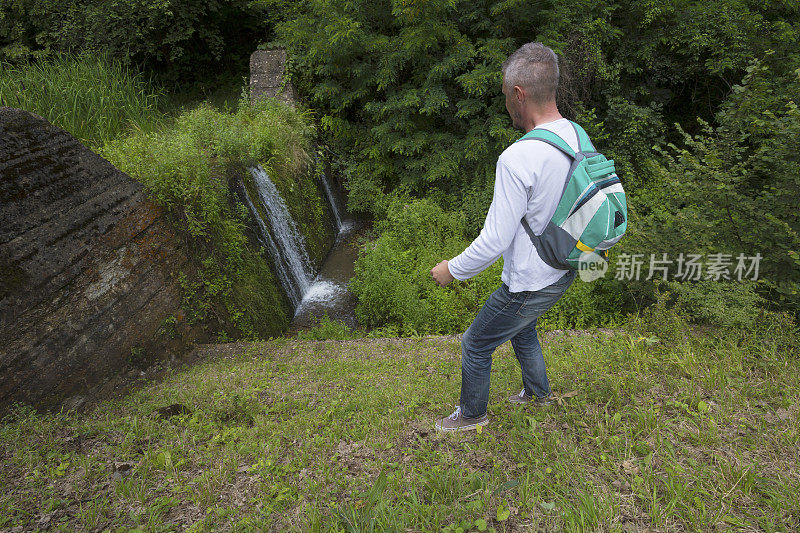 成年男子在小瀑布附近徒步旅行，周围长满了绿色植物