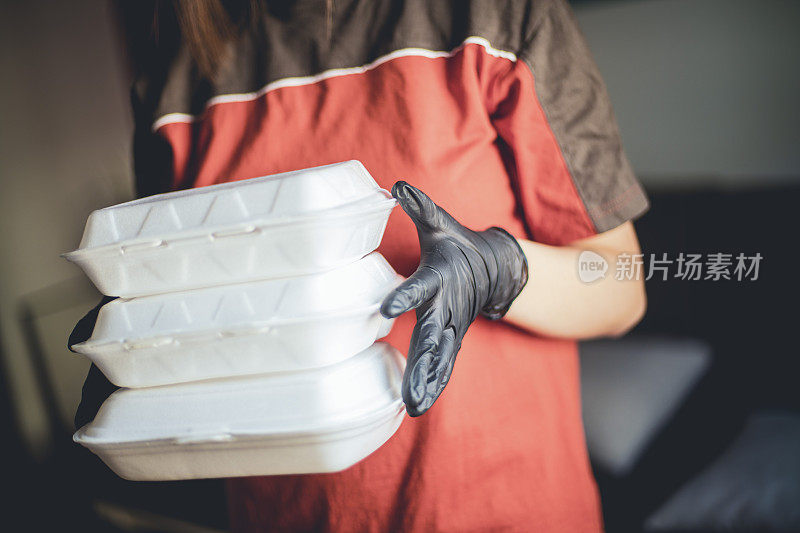 送餐的妇女戴着医用防护口罩和手套拿着食品盒