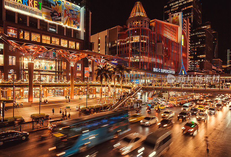 购物中心的灯光照亮了夜晚的城市，道路上的车辆也模糊了灯光的运动