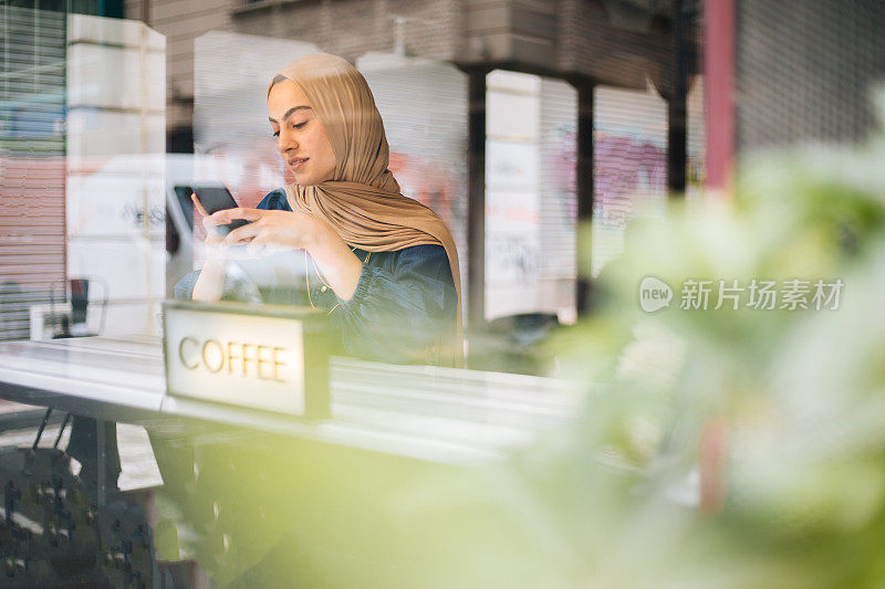 年轻的穆斯林女性在咖啡馆使用智能手机