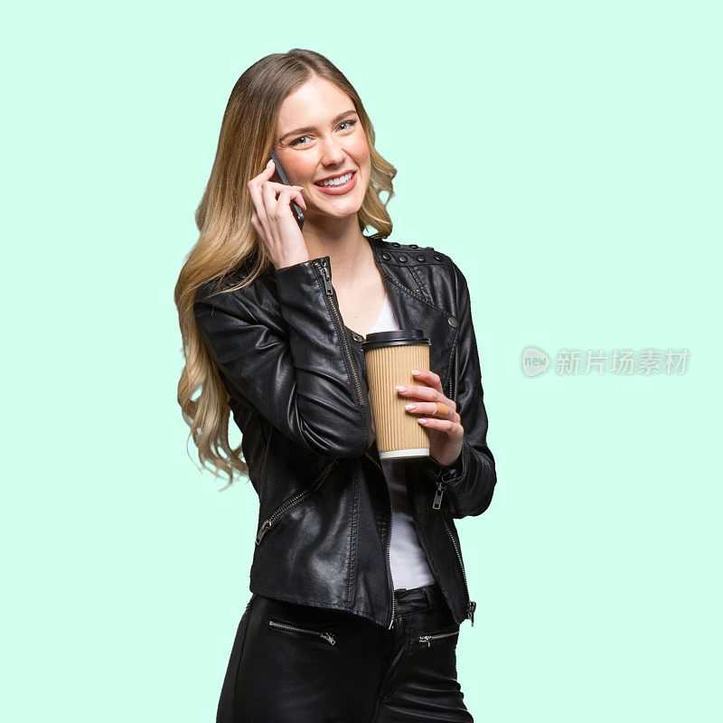 z一代年轻女性穿着衬衫站在白色背景前，拿着咖啡杯，使用手机