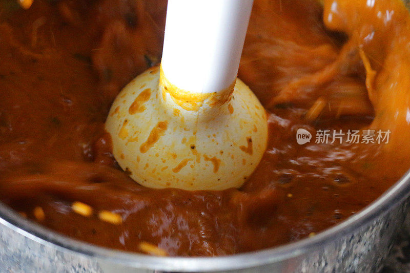 特写图片自制番茄汤煮在平底锅和手工搅拌机混合，高架视图