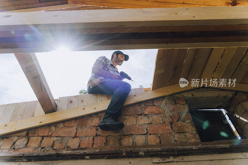 低角度的男性工人坐在木制屋顶上，向下看