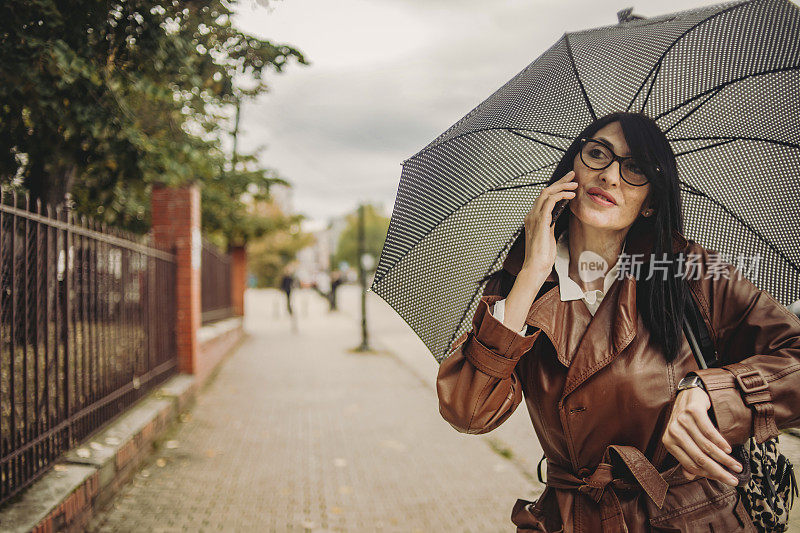 一位漂亮的商务老妇人在雨中行走，手里拿着手机