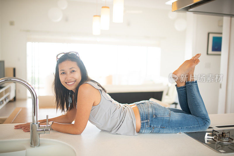 一个快乐的女人躺在厨房的长凳上，在新的现代化的家里
