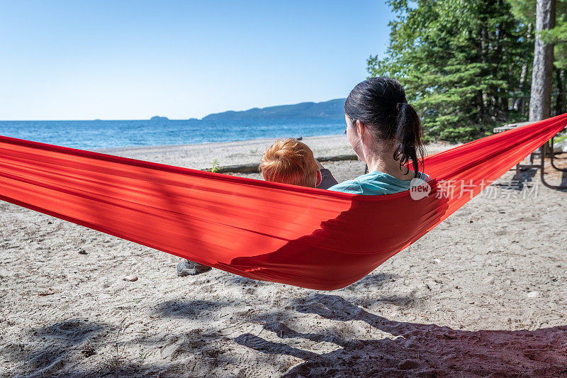 母亲和儿子有乐趣在红色吊床露营在夏天，安大略省，加拿大