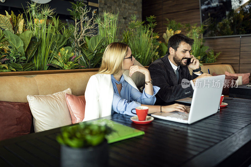 两个商业同事坐在一个咖啡馆和笔记本电脑上工作，享受团队合作和一杯咖啡。
