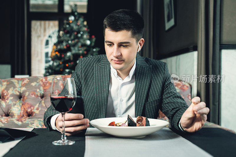 在一家室内餐厅里，一位年轻帅气的男士一边用手机一边吃着烧灰的小牛肉里脊肉和烤蔬菜