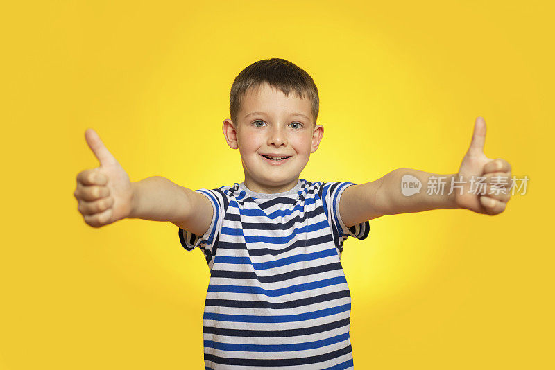 快乐男孩的肖像在条纹t恤显示拇指向上的手势在黄色的背景。