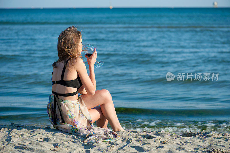 一个年轻的女人坐在沙滩上，手里拿着酒杯