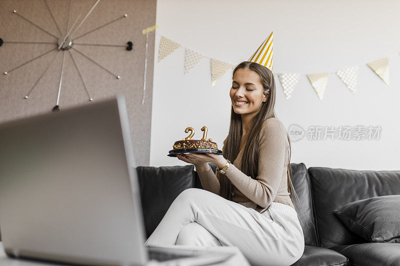 年轻女性在隔离期间在家庆祝生日，并与朋友进行视频通话。她拿着生日蛋糕