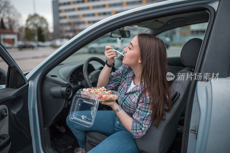 一名女性在停车场吃着塑料容器里的沙拉