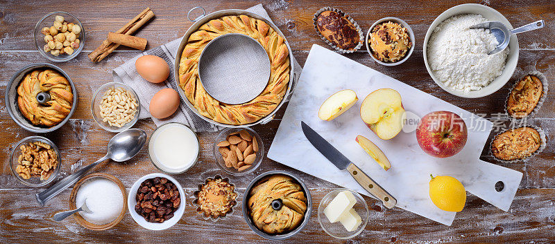 自制的蛋糕，烘烤的糖果与烹饪材料:苹果甜甜圈，松饼和糕点在木制的背景。桌面视图，平放。