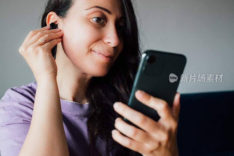 女人戴着无线耳机，拿着智能手机