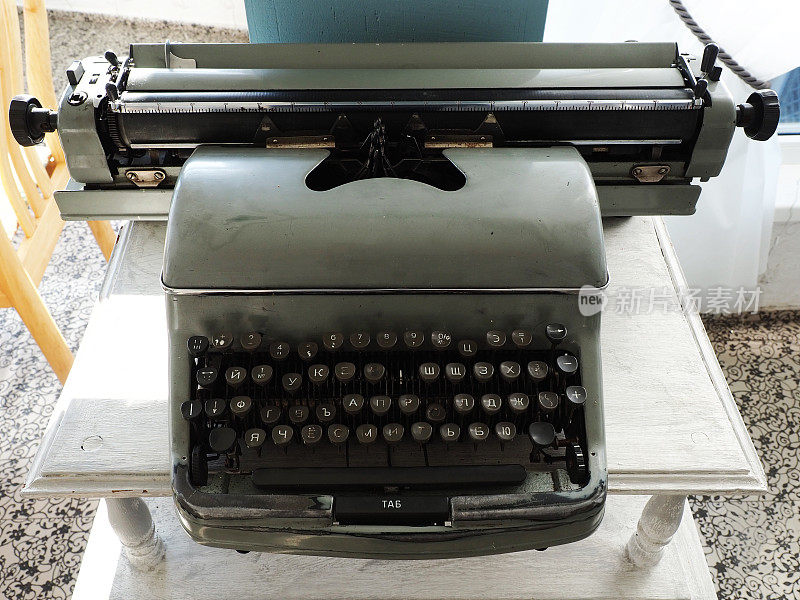 白色木桌上放着一台老式的灰色打字机，上面印着西里尔字母，还有一把丢失的钥匙