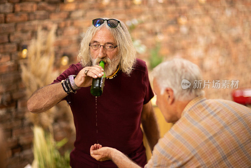 在游园会上，一个老人喝着啤酒，从啤酒瓶里洒了出来，而他的朋友正在用手把啤酒瓶捡起来