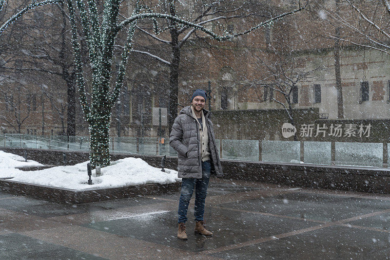 一名男子，一名游客，在纽约市曼哈顿的公园大道上，在大雪中行走在装饰着节日彩灯的树木之间