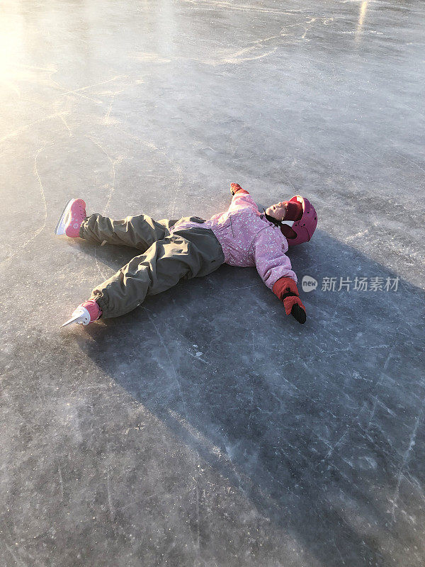 那个孩子正在露天溜冰场上滑冰。孩子累了，仰面躺着。冬天，寒冷的日子和周末的乐趣。