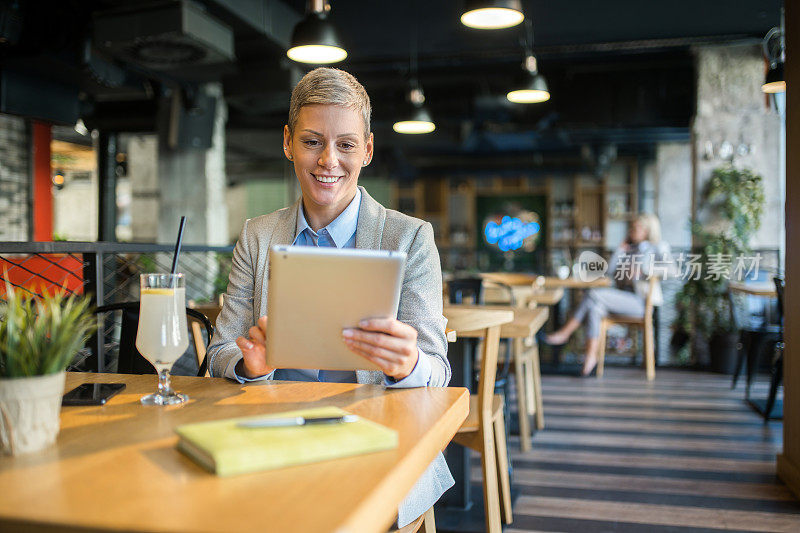 快乐的女经理在咖啡店用平板电脑工作。