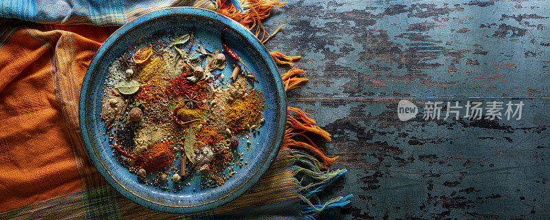 丰富多彩的，有机的，干燥的，充满活力的印度食物香料放在一个古老的青绿色的陶瓷盘上，在一个古老的饱经风霜的木头背景上，还有一个充满活力的颜色对比的桌布。