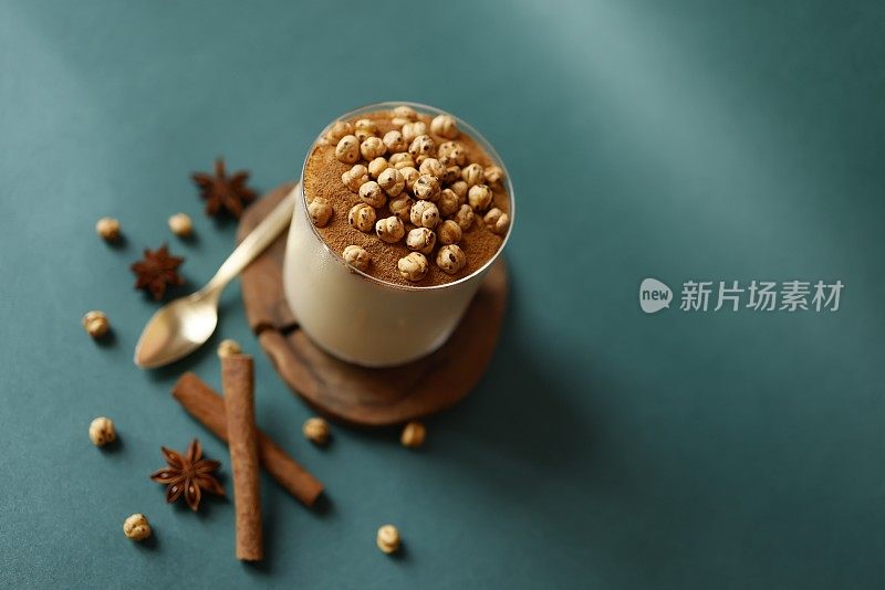 传统土耳其甜点“Boza”，装在玻璃杯里，木制的杯垫上，背景为蓝绿色