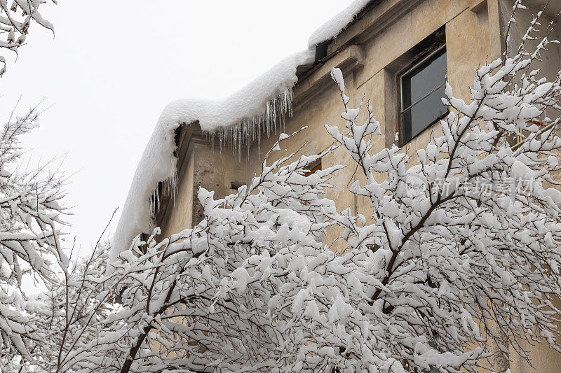 在下雪期间郊区住宅建筑的立面。房子的墙和阳台都被雪覆盖着。在一个寒冷的冬天，树枝被雪覆盖