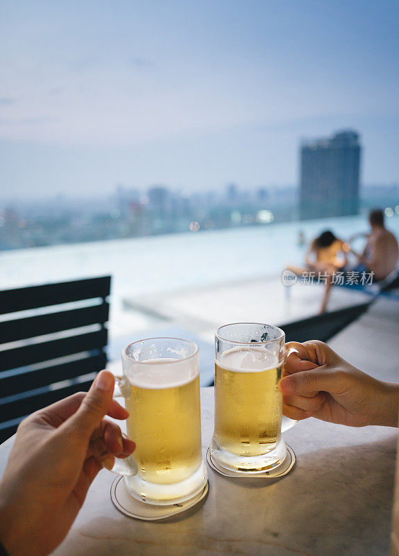 在曼谷的屋顶酒吧享受放松的周五与啤酒在桌子上与泳池的观点