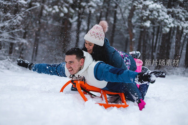 年轻美丽浪漫的夫妇躺在雪橇上在雪地里玩得很开心