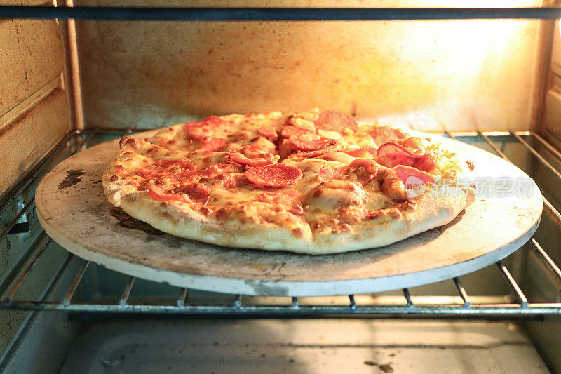 在烤箱中烘烤的自制辣香肠披萨的特写图像，在披萨石头上烤脆的基底，磨碎的马苏里拉奶酪和辣香肠薄片，重点放在前景