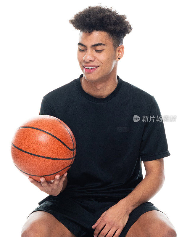 在白色背景前的非裔美国少年穿着运动鞋，手持篮球，使用运动球