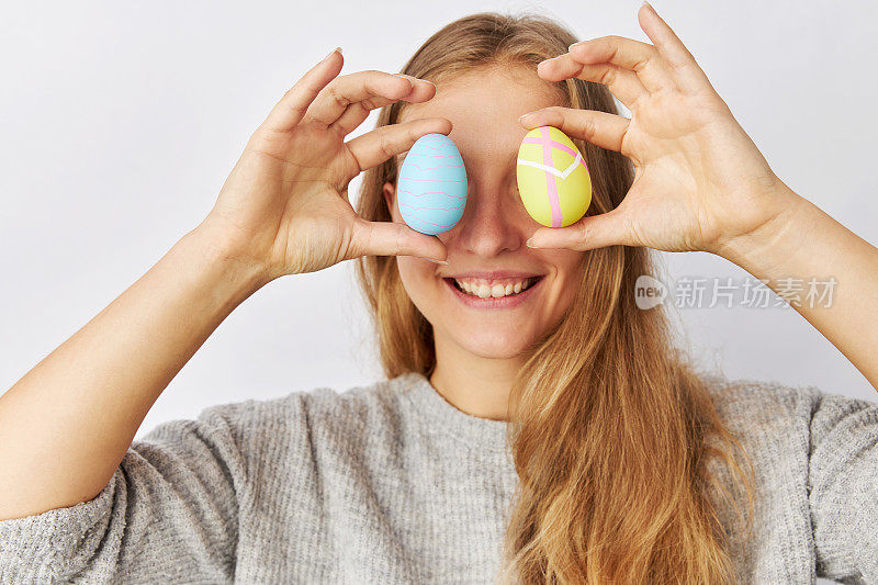 一位金发长发的年轻女子将画好的复活节彩蛋举在眼前