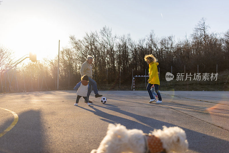 蹒跚学步的孩子和妈妈和爷爷在运动场上踢足球