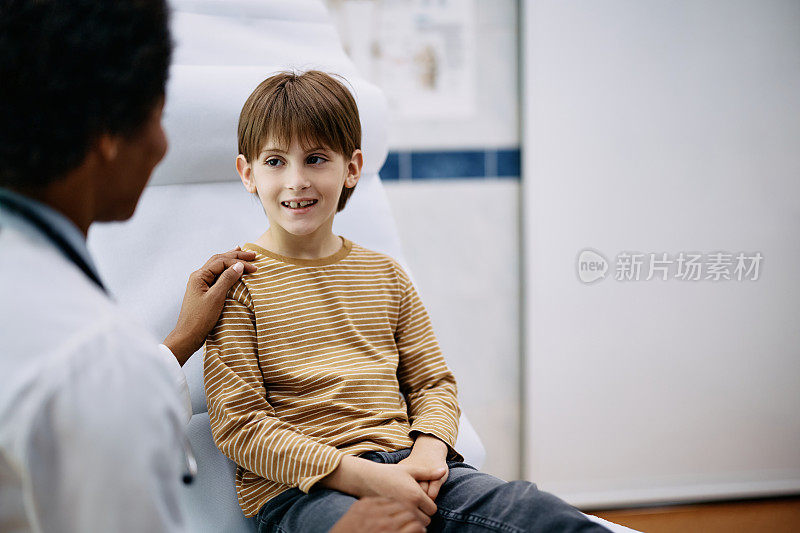 快乐的小男孩在医生办公室体检时和儿科医生说话。